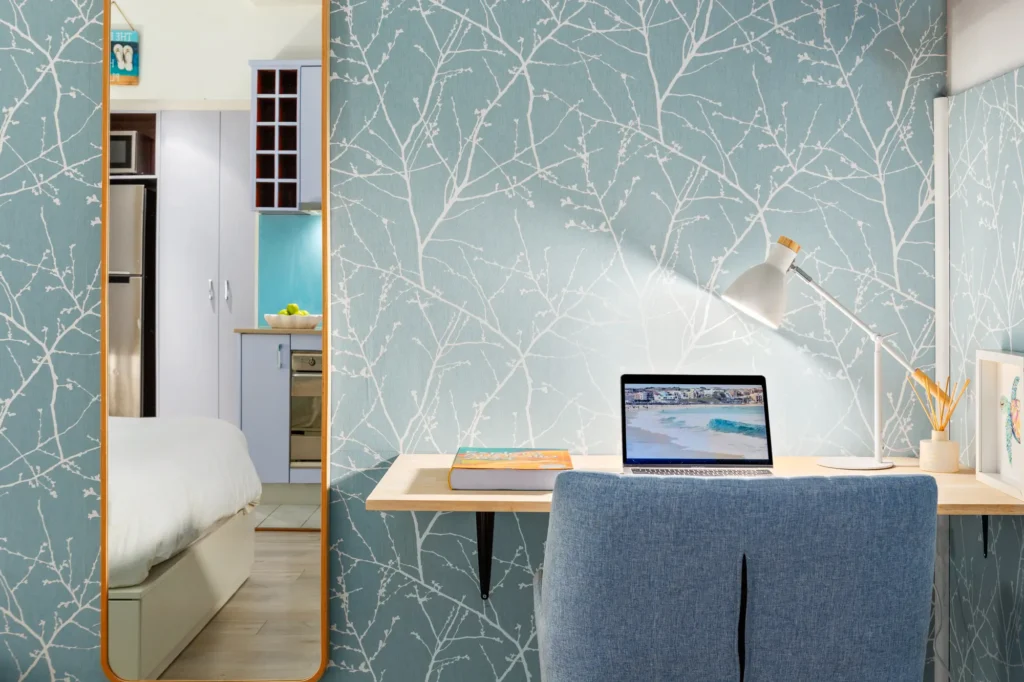 Desk with a laptop and lamp against blue leaf wallpaper beside a mirror in a Bronte short-term rental